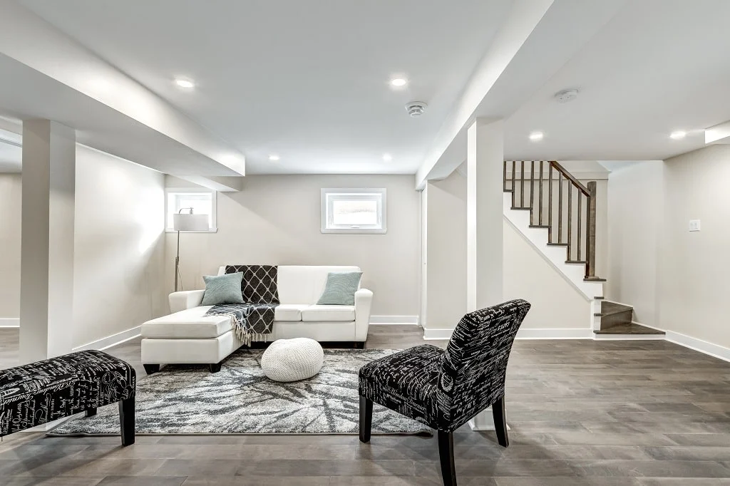 Finished basement lounge with white sectional, light walls and an open staircase
